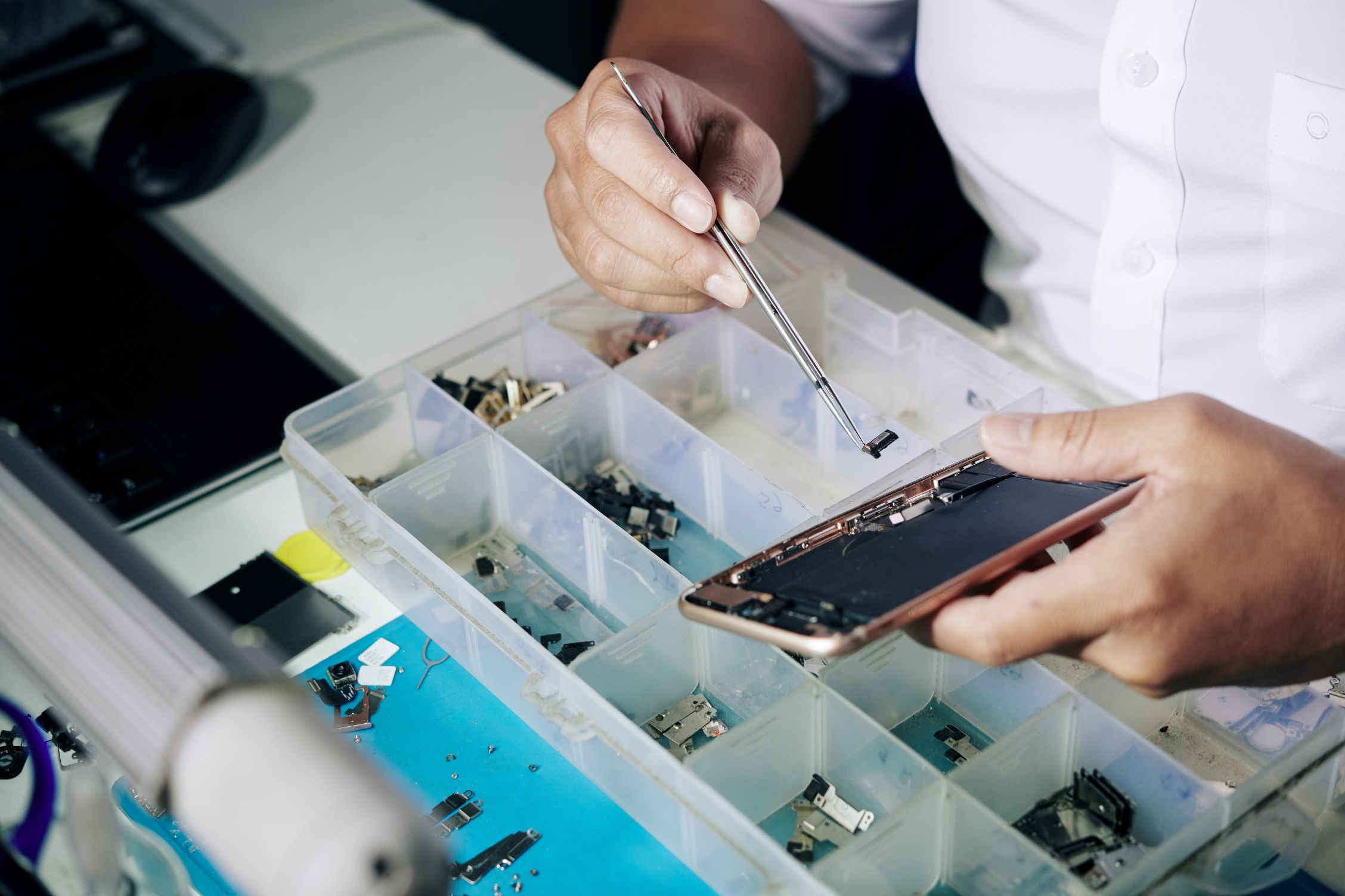 A man is repairing an iPhone screen in a box at One Hour Device Repair.