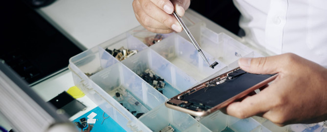 A man is repairing an iPhone screen in a box at One Hour Device Repair. iPhone Screen Repair